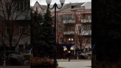 Un locuitor din Herson flutură steaguri ucrainene în fața unei coloane de tancuri parcate n centrul orașului.