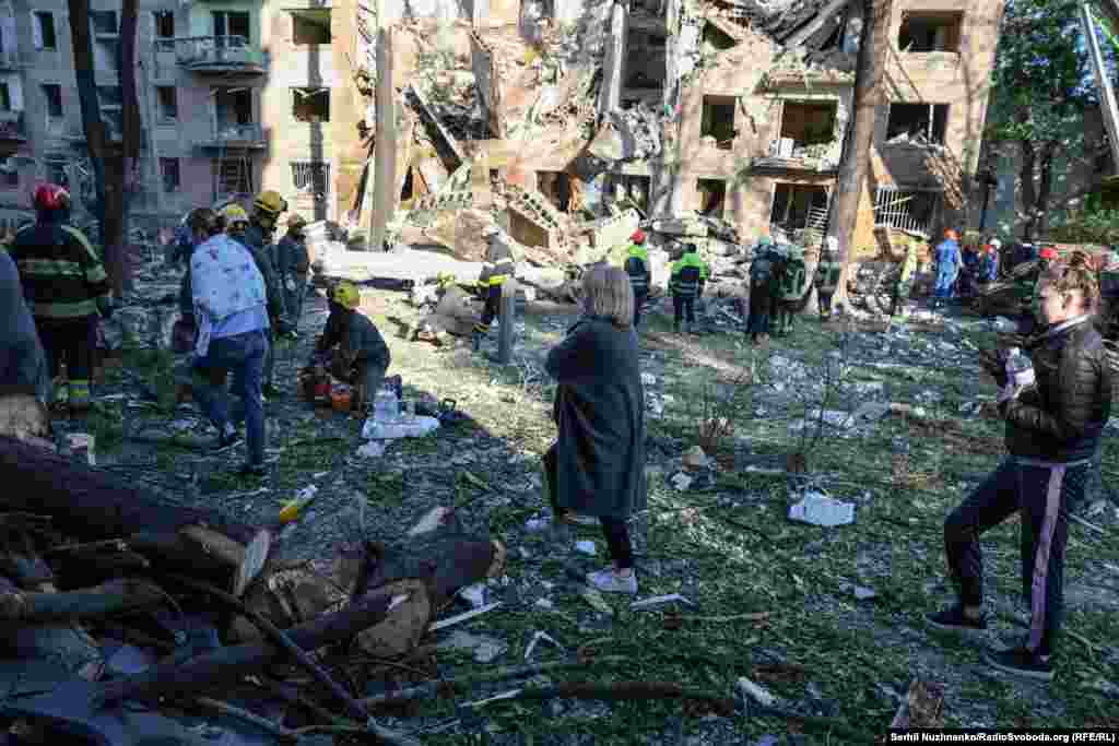 Мешканці напівзруйнованого російською атакою будинку в Києві спостерігають за роботою рятувальників. 23 червня 2025 року