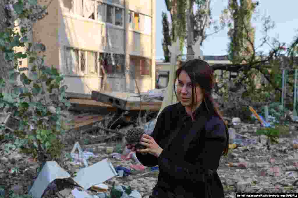 Киянка тримає в руках їжачка, стоячи серед руїн