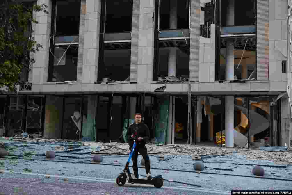 Киянин на самокаті на тлі пошкодженого нежитлового будинку