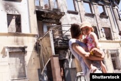 Мама з дитиною біля будівлі в Маріуполі, зруйнованого внаслідок бойових дій у 2014 році, 19 липня 2015 року