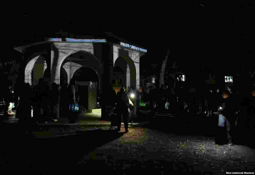 Из-за российских атак в большей части Одессы также отсутствует водоснабжение. На фото: жители Одессы освещают пространство вокруг себя фонариками на телефонах, стоя в очереди, чтобы наполнить бутылки питьевой водой.