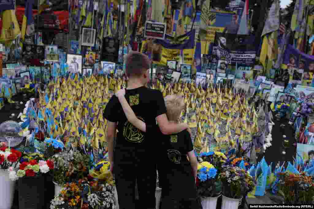 Діти, обійнявшись, дивляться на народний прапорцевий меморіал на Майдані Незалежності в Києві. Липень 2025 року