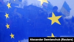Українські протестувальники проглядаються крізь прапор ЄС під час Євромайдану. Київ, 17 грудня 2013 року