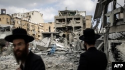 Ультраортодоксальні єврейські чоловіки оглядають пошкодження на місці іранського ракетного удару в Бней-Браку, на схід від Тель-Авіва, 16 червня 2025 року