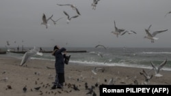 Жінка годує пташок на пляжі Одеси. Попри триваючий для великої частини споживачів блекаут, одесити зберегли своє почуття гумору і оптимізм