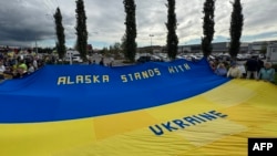 Демонстранты держат гигантский украинский флаг на митинге в поддержку Украины вдоль шоссе Сьюард в Анкоридже, штат Аляска, 14 августа 2025 года, накануне запланированной встречи президентов США и России