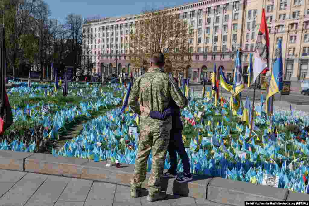Військовий обіймає сина біля народного меморіалу з прапорцями на Майдані Незалежності У Києві. Квітень 2025 року