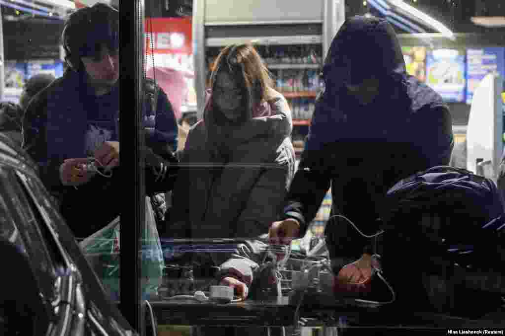 Жители Одессы заряжают свои гаджеты в одном из магазинов, работающих на генераторах, во время отключения электроэнергии, 13 декабря 2025 года. Власти города сообщили, что в результате недавних российских атак пострадала критически важная гражданская инфраструктура.