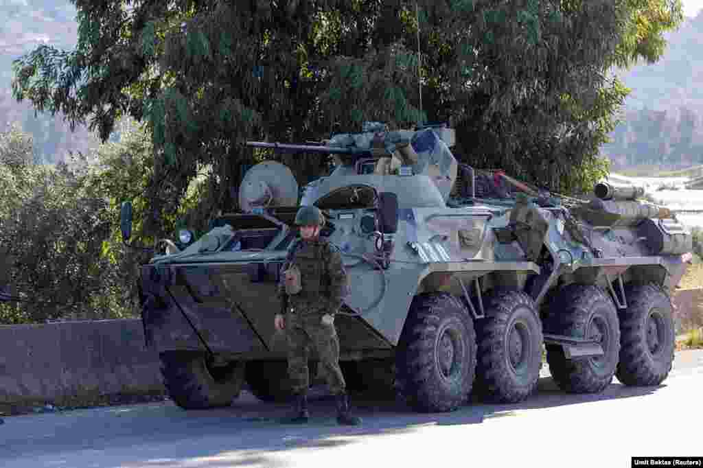 Un soldat rus de gardă lângă un vehicul blindat, în apropierea bazei aeriene Hmeimim. Într-o declarație scrisă despre recenta sa evadare din Siria, președintele alungat de la putere, Bashar Al-Assad, spune că a fost transportat inițial de la Damasc la baza Hmeimim, în timp ce rebelii înaintau rapid spre capitala siriană. În cele din urmă, a fost dus pe calea aerului în Rusia, pe 8 decembrie, după ce baza rusă &bdquo;a fost atacată intens cu ajutorul dronelor&rdquo;.