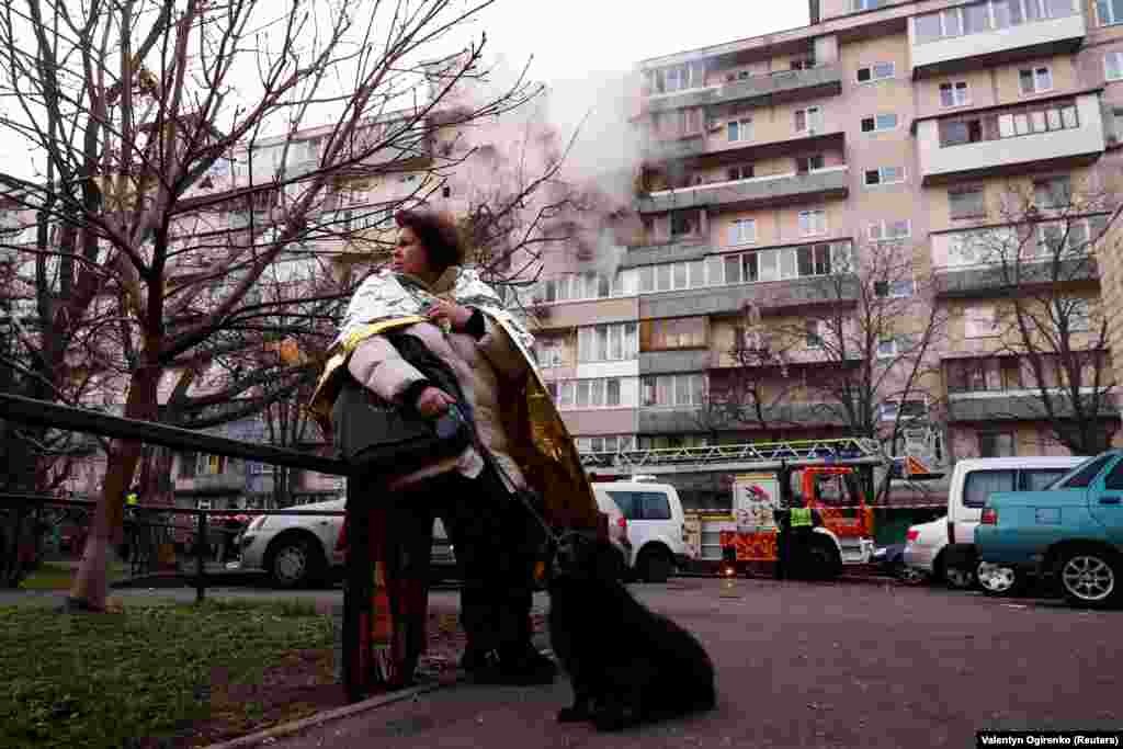 Женщина стоит с собакой рядом с жилым домом, пострадавшим в результате ночного удара российского беспилотника и ракеты на фоне нападения России на Украину, в Киеве, Украина, 14 ноября 2025 года. REUTERS/Валентин Огиренко